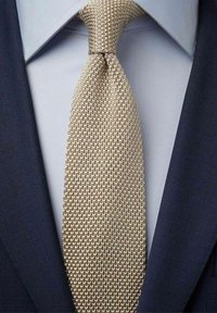 Neuleolki vaalean kullanvärisenä, jossa on tekstuuri, käytetty vaaleansinisellä paidalla tumman laivastonsinisen takin alla. Lähikuva.