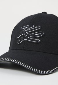 Casquette de baseball en laine noire avec un logo brodé blanc, des coutures contrastantes le long de la visière et un design de couronne arrondie.