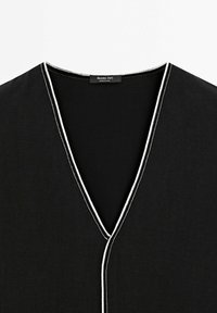 Top noir à col en V avec un liseré blanc le long de l'encolure et de l'ouverture frontale, avec une étiquette Massimo Dutti à l'intérieur du col.