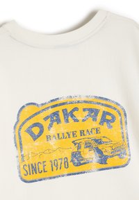 Biała bawełniana koszulka z efektem postarzania, z niebiesko-żółtym grafiką Dakar Rally Race, zawierająca rok 1978 oraz ilustrację pojazdu rajdowego.