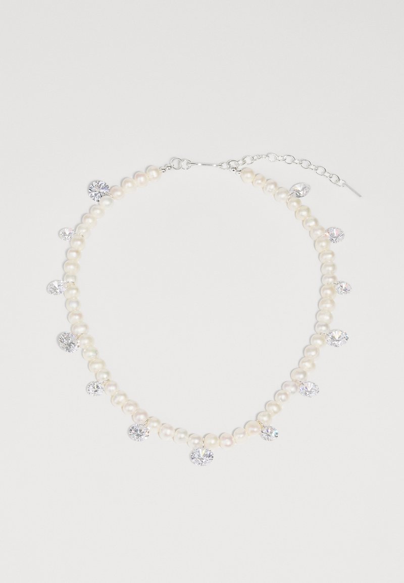 Πετσέτα από μαργαρίτα με μεταλλική λαβή σε ασημί απόχρωση, διαθέτοντας ομοιόμορφα κατανεμημένες κρυστάλλινες λεπτομέρειες ανάμεσα σε λαμπερά λευκά μαργαριτάρια. Ρυθμιζόμενη αλυσίδα για μήκος.