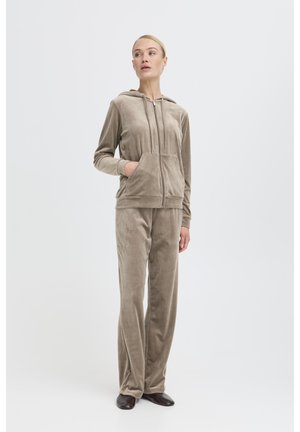 Ensemble en velours dans un taupe doux. Le hoodie zippé présente une poche avant, tandis que le pantalon a une coupe décontractée et une texture lisse.