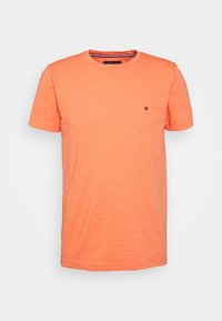 Krátký rukáv, oranžové tričko z jemné texturované látky; má malé logo na hrudi a kulatý výstřih.