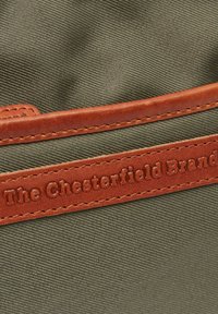 Borsa in tessuto verde oliva con un accento in pelle marrone liscia che mostra "The Chesterfield Brand" impresso nella pelle.