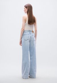 Φαρδιά τζιν παντελόνια σε ανοιχτό μπλε χρώμα από τζιν ύφασμα, με καφέ δερμάτινο ταμπελάκι στο πίσω μέρος, απλές πίσω τσέπες και άνετη εφαρμογή.