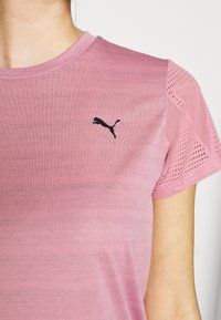 Woman wearing a pink Puma athletic shirt with mesh short sleeves and a black Puma logo on the chest.
