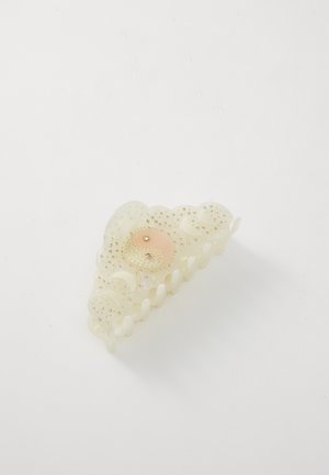 Puikiai skaidrus plaukų segtukas kremiško atspalvio, su banguota dizaino struktūra. Jame yra centrinis persikų spalvos akcentas ir smulkūs dekoratyviniai karoliukai.