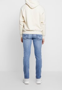 Světle modré džíny z denimu s rovnými nohavicemi, doplněné krémově zbarvenou mikinou s kapucí, pohled zezadu.