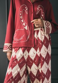 Rote Bluse mit einem Schwanendesign und weißen Herzakzenten, kombiniert mit hoch taillierten Hosen mit schwanenförmigen Diamantmustern in Rot und Creme.