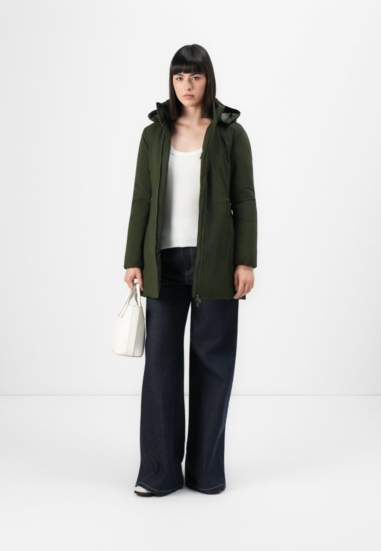 Veste matelassée vert olive avec capuche, fermeture éclair et poches latérales, associée à un jean large taille haute bleu foncé et à un sac blanc.