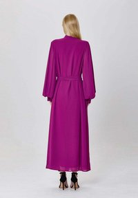 Robe longue et fluide de couleur magenta avec une ceinture, des manches bouffantes et une texture lisse. Le design présente un col ajusté et une longueur mi-mollet.