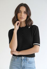 Czarna dzianinowa koszulka polo z krótkimi rękawami; posiada białe paski na mankietach i trzy guziki przy kołnierzu. Noszona z jasnoniebieskimi dżinsami.