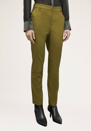 Pantalones de corte ajustado en verde oliva con una textura suave, con un frente plano y bolsillos laterales. Llevados con tacones negros de punta.