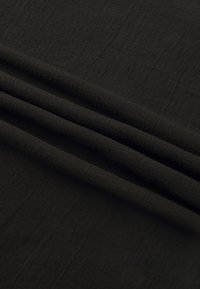 Svart teksturert stoff med myk, litt ruglete overflate, falt i lag, som viser materialet og den matte finishen.