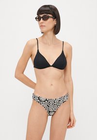 Μαύρο ριγωτό μπικίνι τοπ σε σχήμα τριγώνου με λεπτές τιράντες, συνδυασμένο με μπικίνι κάτω μέρος σε μαύρο και άσπρο σχέδιο με γεωμετρικά μοτίβα.