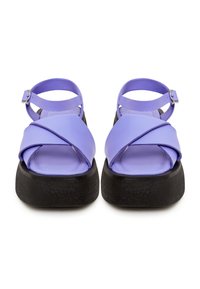 Sandali in pelle viola con design a fascia incrociata e fibbia alla caviglia, dotati di una suola spessa nera texturizzata. Stile aperto davanti.