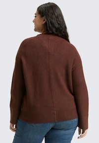 Bruine geribbelde trui met een relaxed fit, lange mouwen en een naad in het midden van de rug, gecombineerd met blauwe jeans voor een casual look.