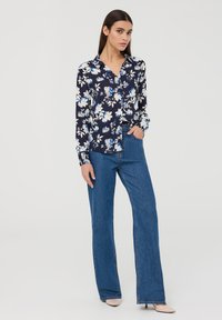 Blusa floreale a maniche lunghe in tessuto blu navy con motivi bianchi e blu. Abbinata a jeans ampi a vita alta in blu chiaro e scarpe neutre.