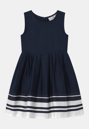 Vestido sin mangas de color navy con falda plisada y rayas horizontales blancas cerca del dobladillo, que cuenta con un escote redondo y cremallera en la espalda.