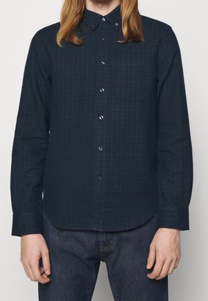 Chemise à manches longues bleue marine avec un col à bouton, présentant un motif rayé subtil et une poche poitrine unique. Fabriquée en tissu texturé.