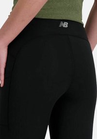 Leggings neri con una texture liscia, dotati di una vita alta e di un logo riflettente sul retro vicino alla vita.