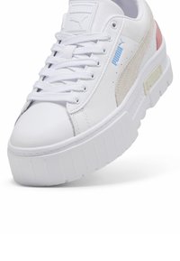 White platform sneakers made of leather and suede, featuring a textured sole, round toe, and a light pink accent on the heel.