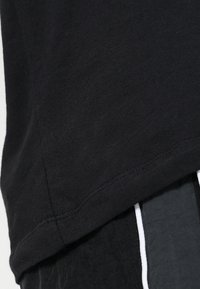 Camiseta negra de algodón con una textura suave, con un dobladillo curvado. El diseño incluye detalles de costura sutiles.