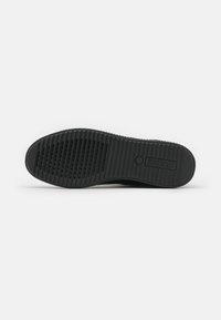 Black rubber shoe sole featuring a textured surface, multiple grooves, and a circular logo detail for grip and support.