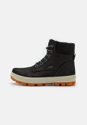 Zwarte suède enkellaars met een beige rubberen zool en een oranje antislipzool. Voorzien van blauwe veters en stiksels, met een gevoerde schacht voor comfort.
