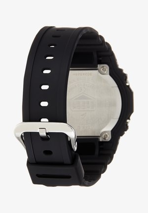 Digitalur med sort silikonerem, sølvfarvet metalspænde og bagside i rustfrit stål med indgraverede detaljer.