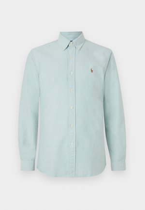 Gai zils pogājamo krekliņš ar apkakli, garām piedurknēm un mazu izšūtu logo uz krūtīm. Izgatavots no mīkstas, teksturētas auduma.