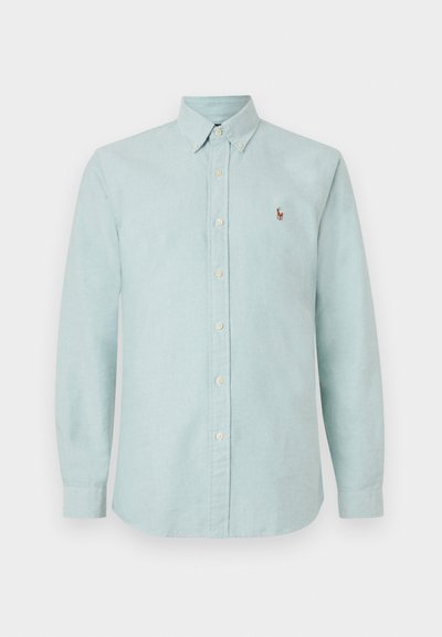 Šviesiai mėlyna marškinėlių mygtukų su apykakle, ilgomis rankovėmis ir maža siuvinėta logotipu ant krūtinės. Pagaminta iš minkštos, tekstūruotos medžiagos.