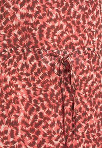 Červená a růžová látka s vzorem, která obsahuje nepravidelné černé akcenty, s detailem na šňůrku v pase pro nastavitelné přizpůsobení.