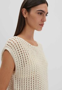 Gehaakte top in gebroken wit, met een losse pasvorm, brede halslijn en een textuurpatroon met open weefsels. Casual en lichtgewicht ontwerp.