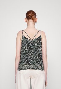 Débardeur noir à fleurs avec des bretelles fines, présentant un motif de petites fleurs pastel. Tissu doux avec une coupe ample et un délicat détail au dos.