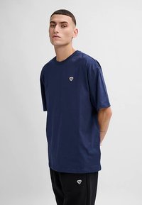 Mörkblå kortärmad t-shirt i bomullstyg med en liten dekorativ logotyp på bröstet. Casual passform, enkel design och slät textur.