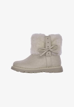 Beige enkellaars met een zachte bontkraag, gestructureerde buitenkant, platte rubberen zool, strik en hartvormige accenten aan de zijkant.