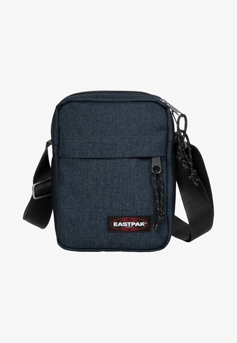 Tmavě modrá látková crossbody taška s nastavitelným popruhem, zipovou přední kapsou a logem Eastpak. Má oblý tvar a strukturovaný povrch.