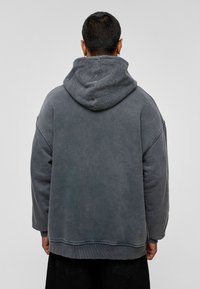 Grijze oversized hoodie met een gestructureerde, donkergrijze fleece-voering aan de capuchon. Heeft druppelschouders en ribgebreide manchetten, met een casual, relaxte pasvorm.