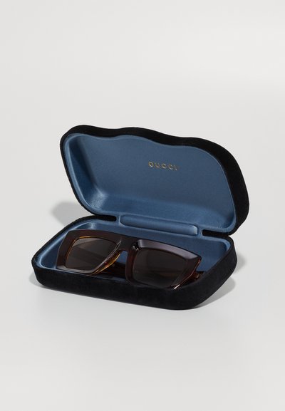 Gucci napszemüveg fekete bársonytokban, sötét lencsékkel és négyzet alakú kerettel, barna teknőspáncél mintával, kék belső térrel.