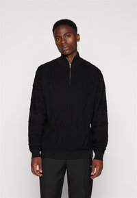 Black knitted pullover with a half-zip collar. Features textured cable patterns and ribbed cuffs and hem. Classic fit style.