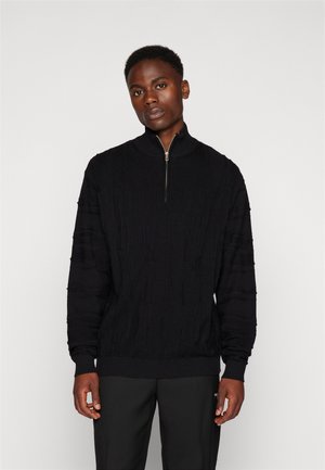 Black knitted pullover with a half-zip collar. Features textured cable patterns and ribbed cuffs and hem. Classic fit style.