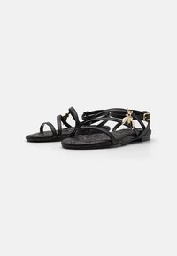Sorte sandaler med flere tynne reimer og en teksturert såle. Har et gullcharmsdekor. Flat design med en sikker ankelreim.