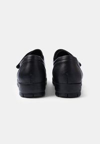 Chaussures noires en cuir avec une forme arrondie, dotées d'un talon bas et d'accents en tissu texturé sur le côté. Finition lisse avec des coutures visibles.
