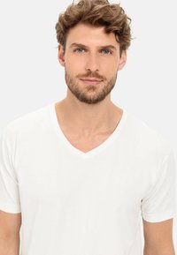 Hvid v-hals t-shirt lavet af blødt stof, korte ærmer og en afslappet pasform. Glat tekstur uden synlige mønstre eller accenter.