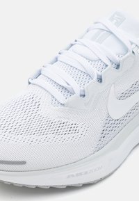 Gros plan d'une chaussure de course Nike blanche avec une tige en mesh, des lacets blancs et un amorti Air Zoom visible sur la semelle.