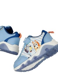 Baskets enfant bleu clair avec des personnages de chien de dessin animé sur le côté, fermeture scratch et languette orange au talon.