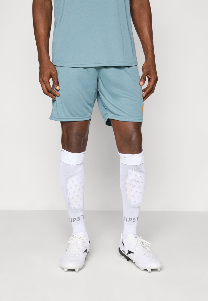 Athletic outfit featuring a light blue moisture-wicking shirt and matching shorts. White knee-high socks with padding and black soccer cleats.