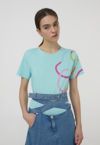 T-shirt azzurro chiaro a maniche corte con motivi astratti multicolori. Abbinato a una gonna di jeans con una cintura a struttura incrociata.