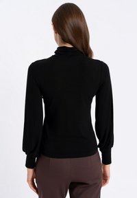 Czarny top z długim rękawem i wysokim kołnierzem, z marszczeniami na ramionach i dopasowanymi mankietami, wykonany z gładkiej, elastycznej tkaniny.